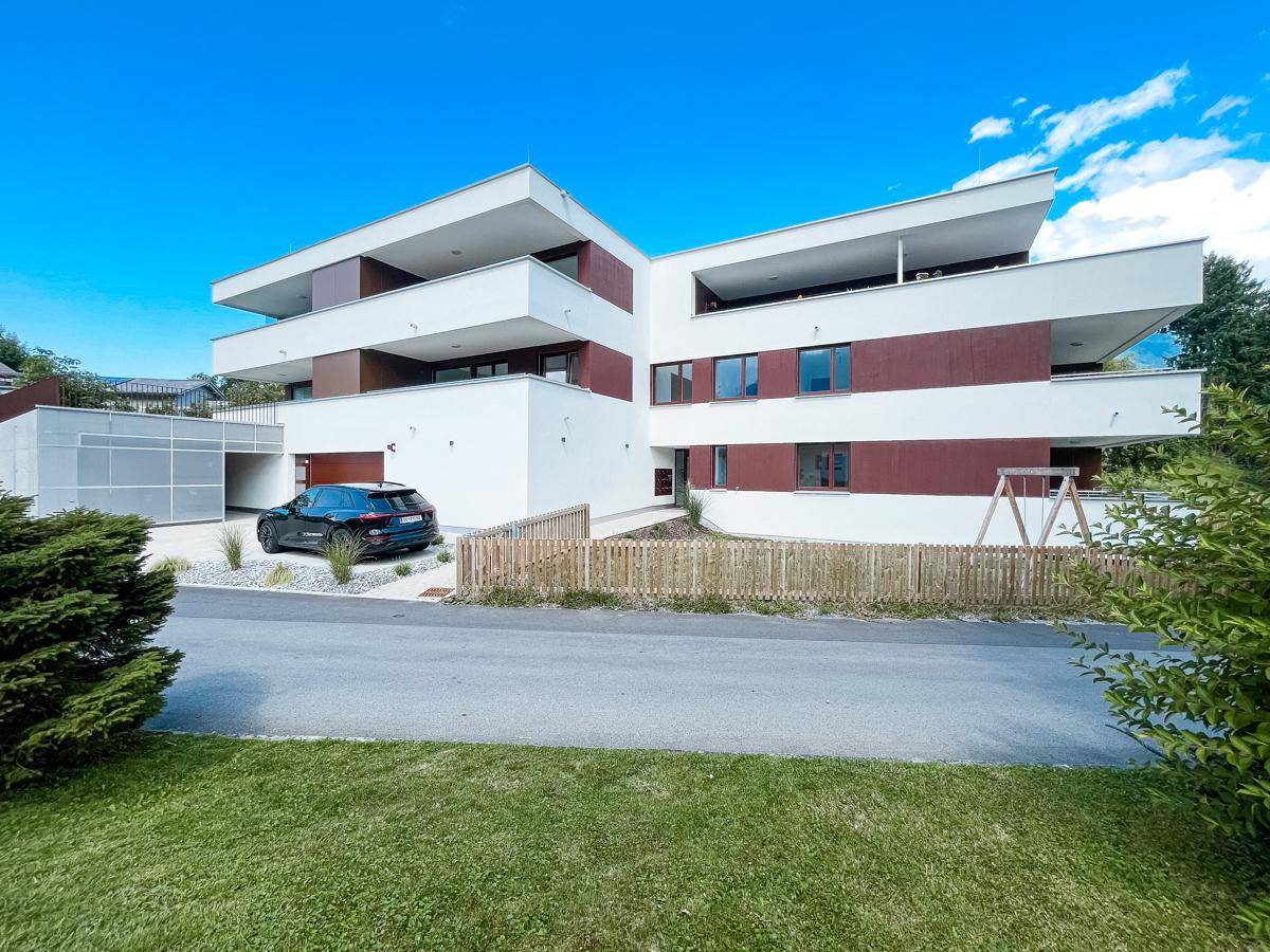 Gesamtansicht des modernen Wohnkomplexes mit Balkonen, Parkplatz und einem kleinen Spielbereich.