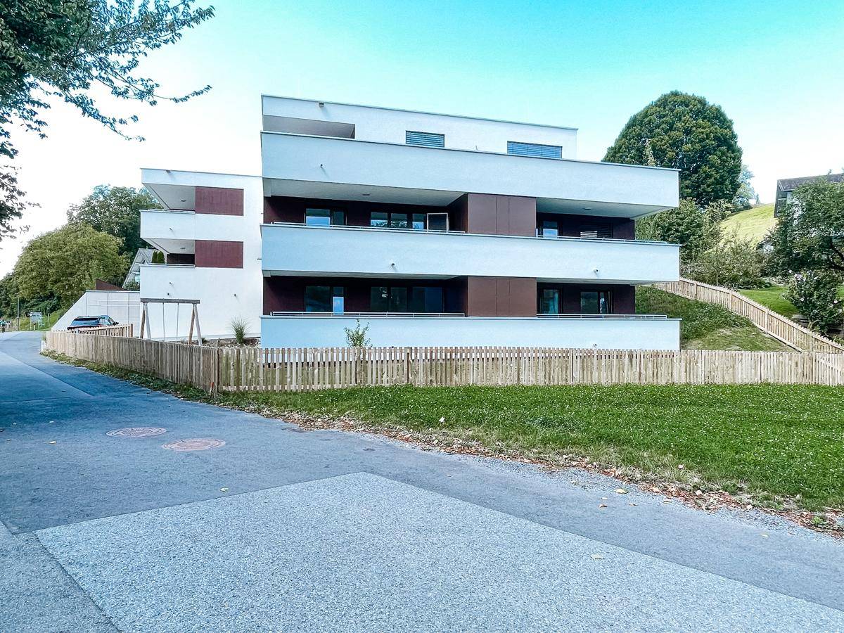 Modernes Mehrfamilienhaus mit klaren Linien, Balkonen und einer Holzumzäunung im Vordergrund.