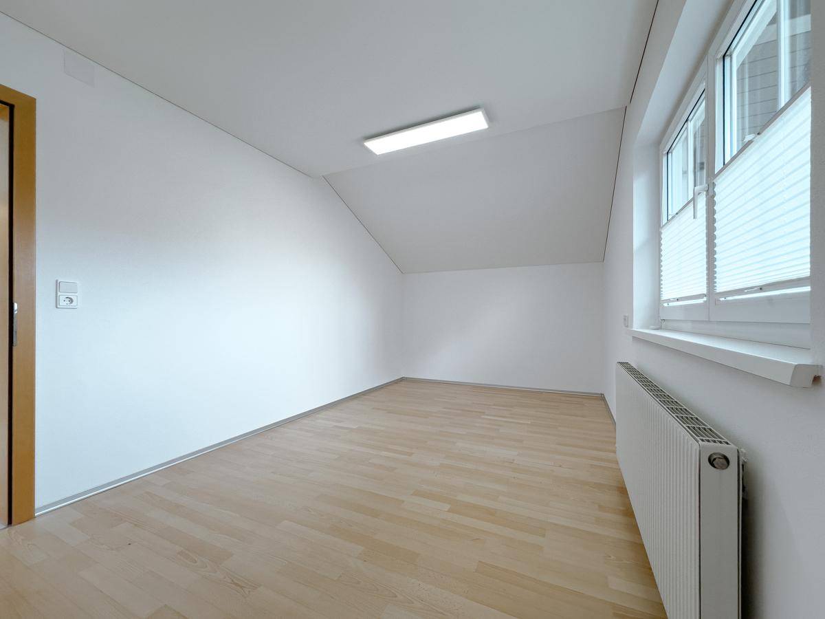 Helles Zimmer im Dachgeschoss mit Laminatboden, Dachschräge und Fenster.