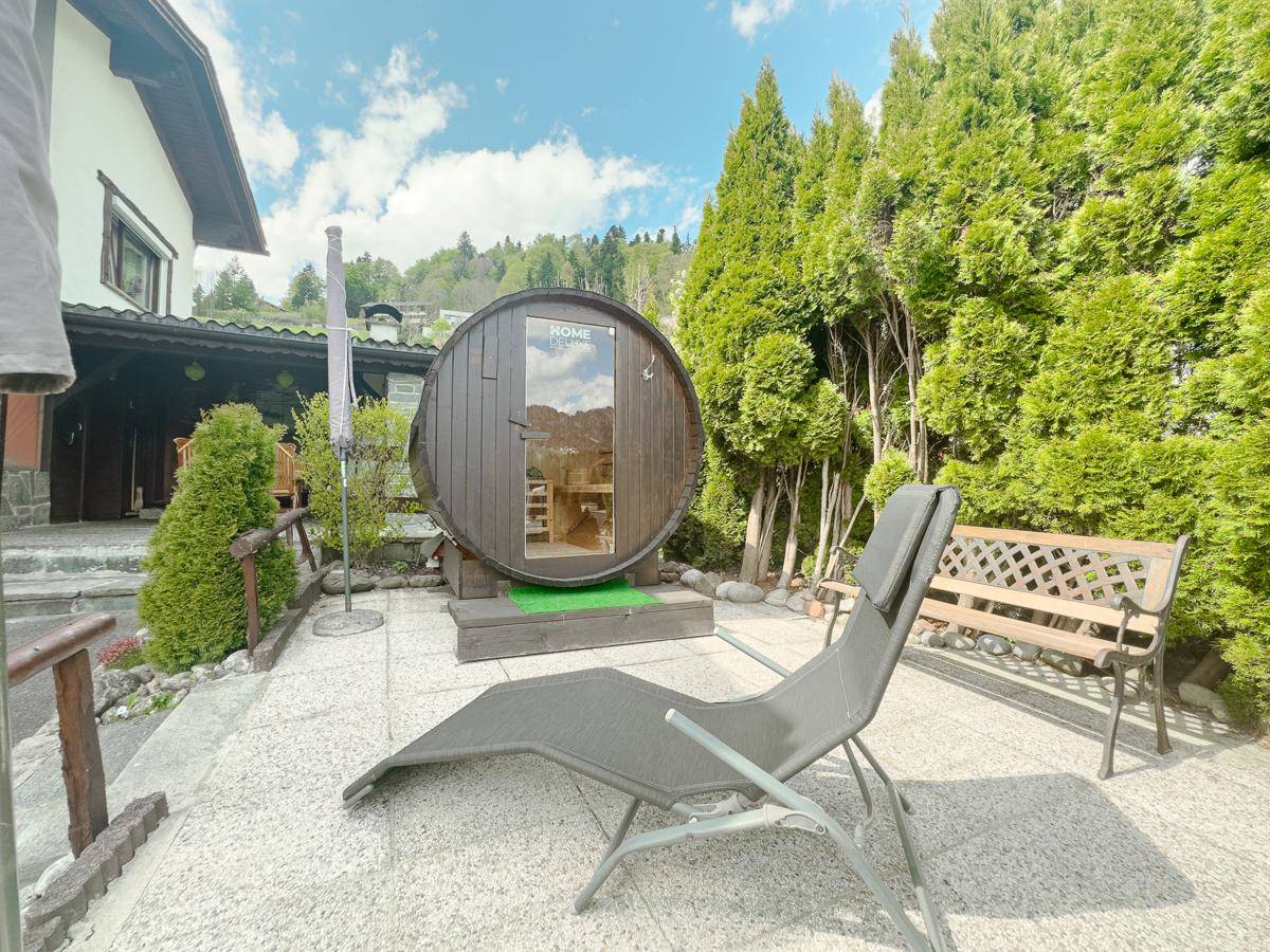 Entspannungsbereich im Garten mit Fasssauna, Liegestuhl und Blick auf die grüne Landschaft.