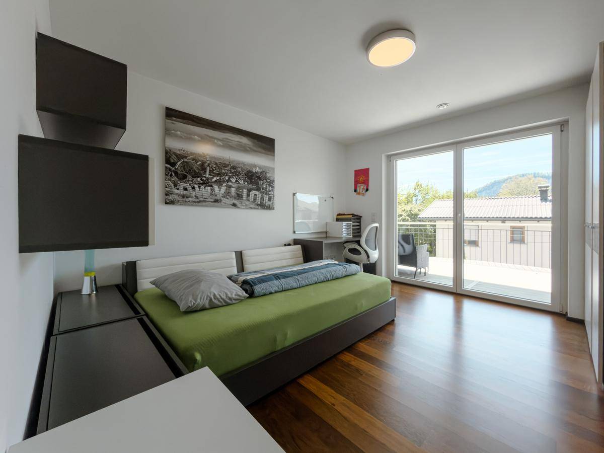 Schlafzimmer mit Balkonzugang, modernem Bett und Schreibtisch, bietet viel Tageslicht.