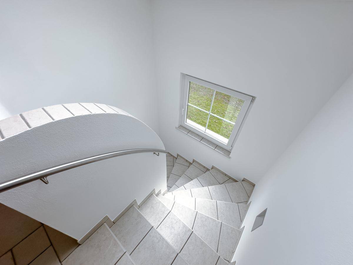 Wendeltreppe mit Fliesenstufen und Fenster, die die oberen Etagen verbindet.