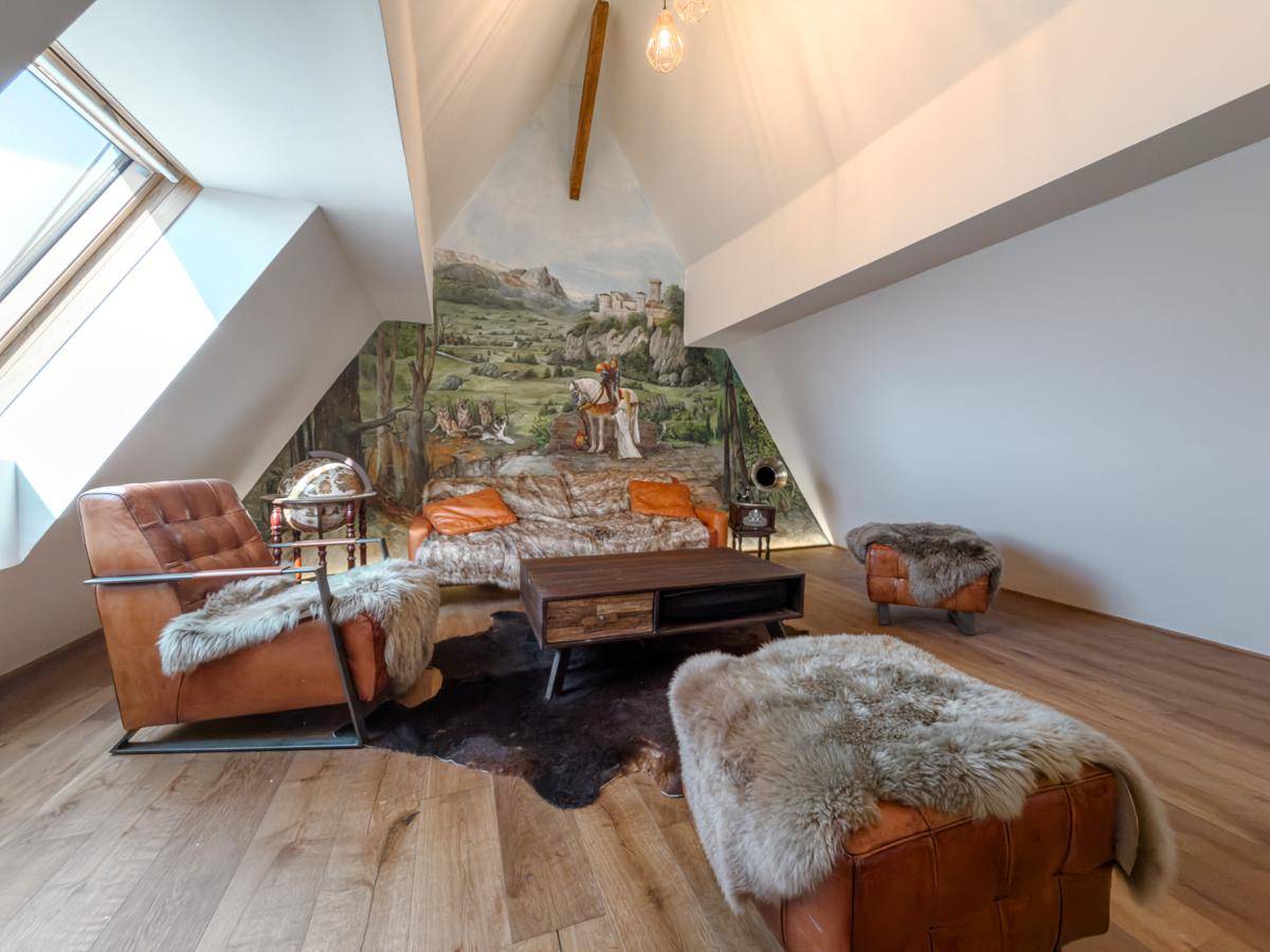 Gemütliches Wohnzimmer im Dachgeschoss mit Holzboden, Dachschrägen und einer Wandmalerei.