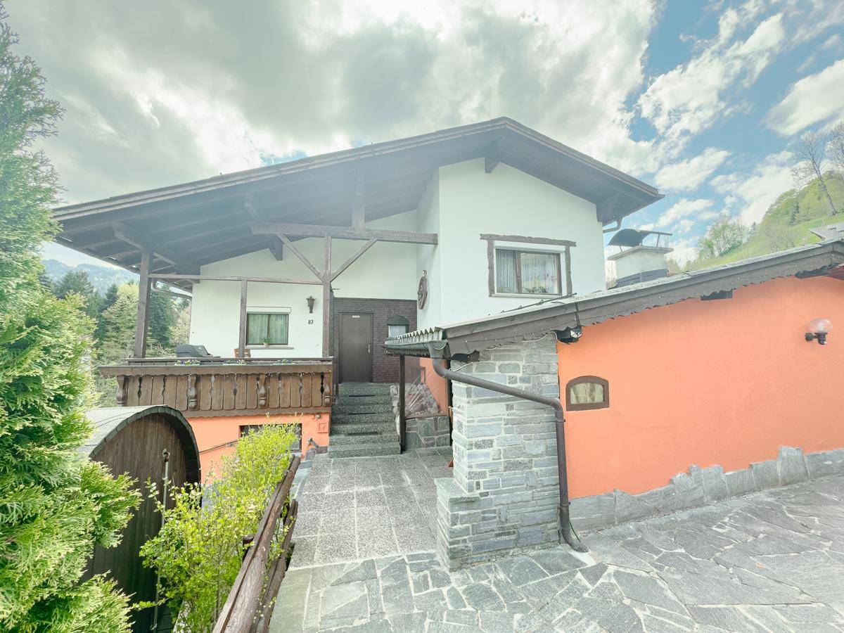 Haupteingang des Hauses mit Steinfliesenweg und traditioneller Holzverkleidung am Balkon.