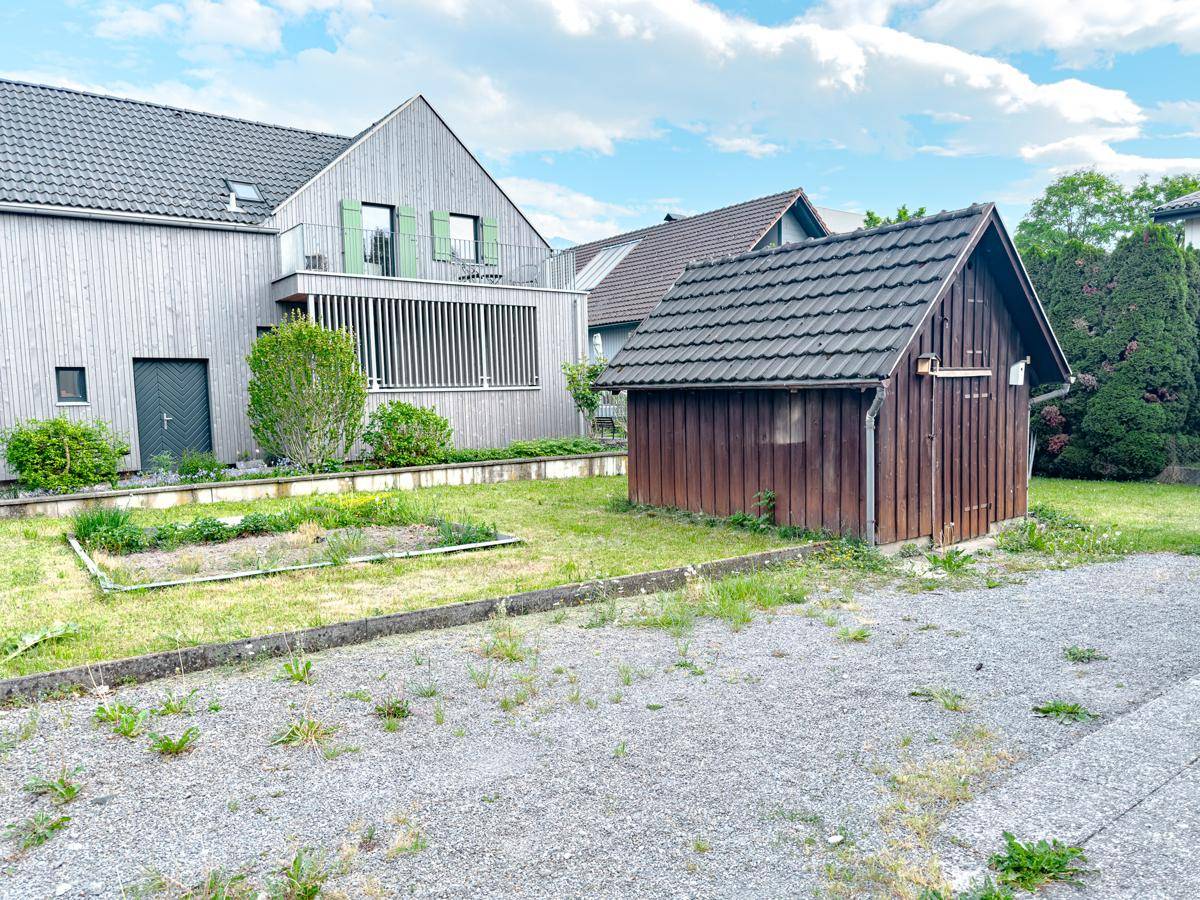 Gartenbereich mit Holzschuppen, Kiesfläche und angrenzendem modernen Nachbarhaus.