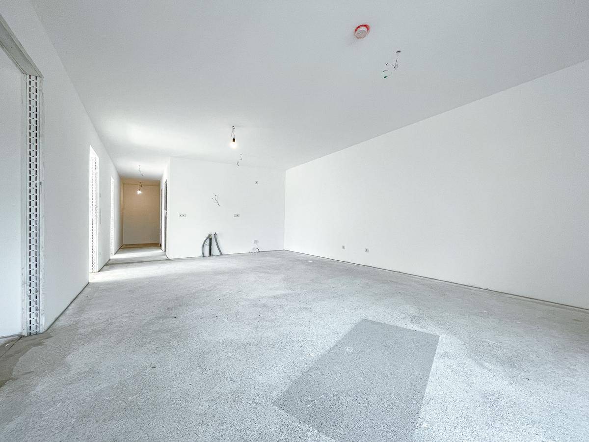 Großzügiger, heller Wohnbereich im Rohbau mit weißen Wänden und Estrichboden, ideal für offene Gestaltung.