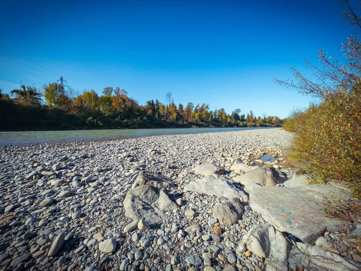 Flusslandschaft mit weitem Kiesstrand und bewaldetem Ufer unter blauem Himmel.