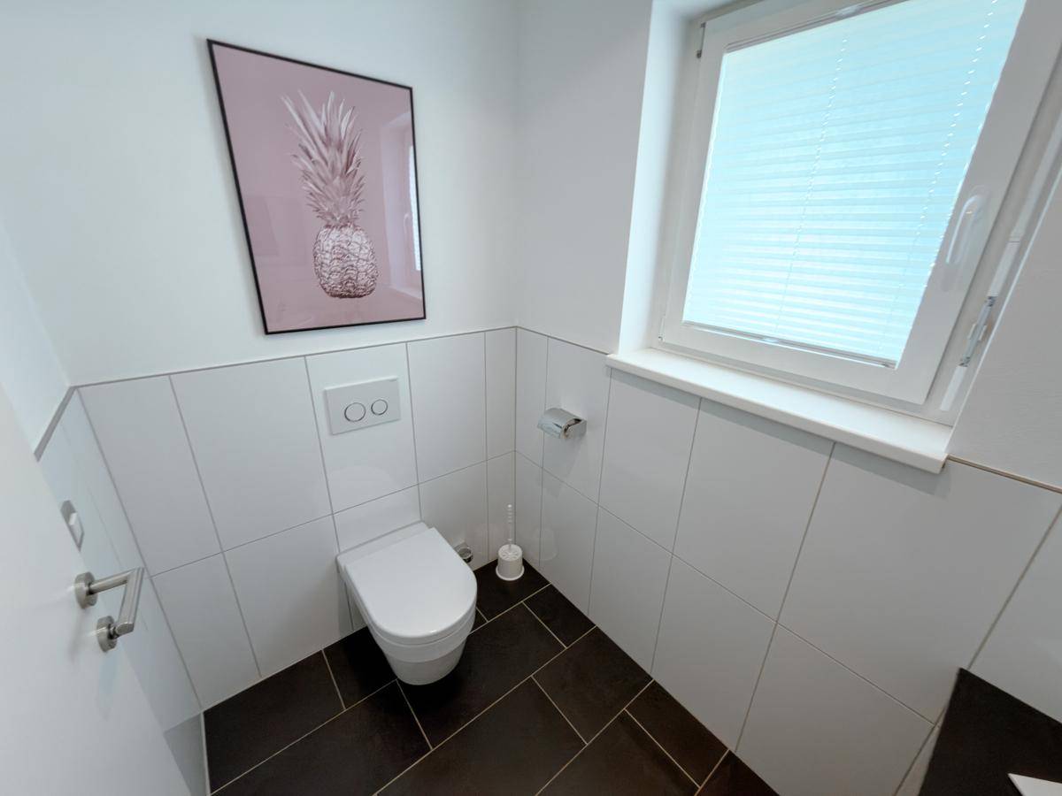 Helles Gäste-WC mit Fenster, Wand-WC und moderner Fliesenverkleidung.