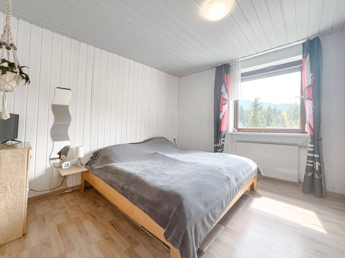 Schlafzimmer mit Holzboden, Fenster und Vorhängen, bietet einen weiten Blick in die Landschaft.