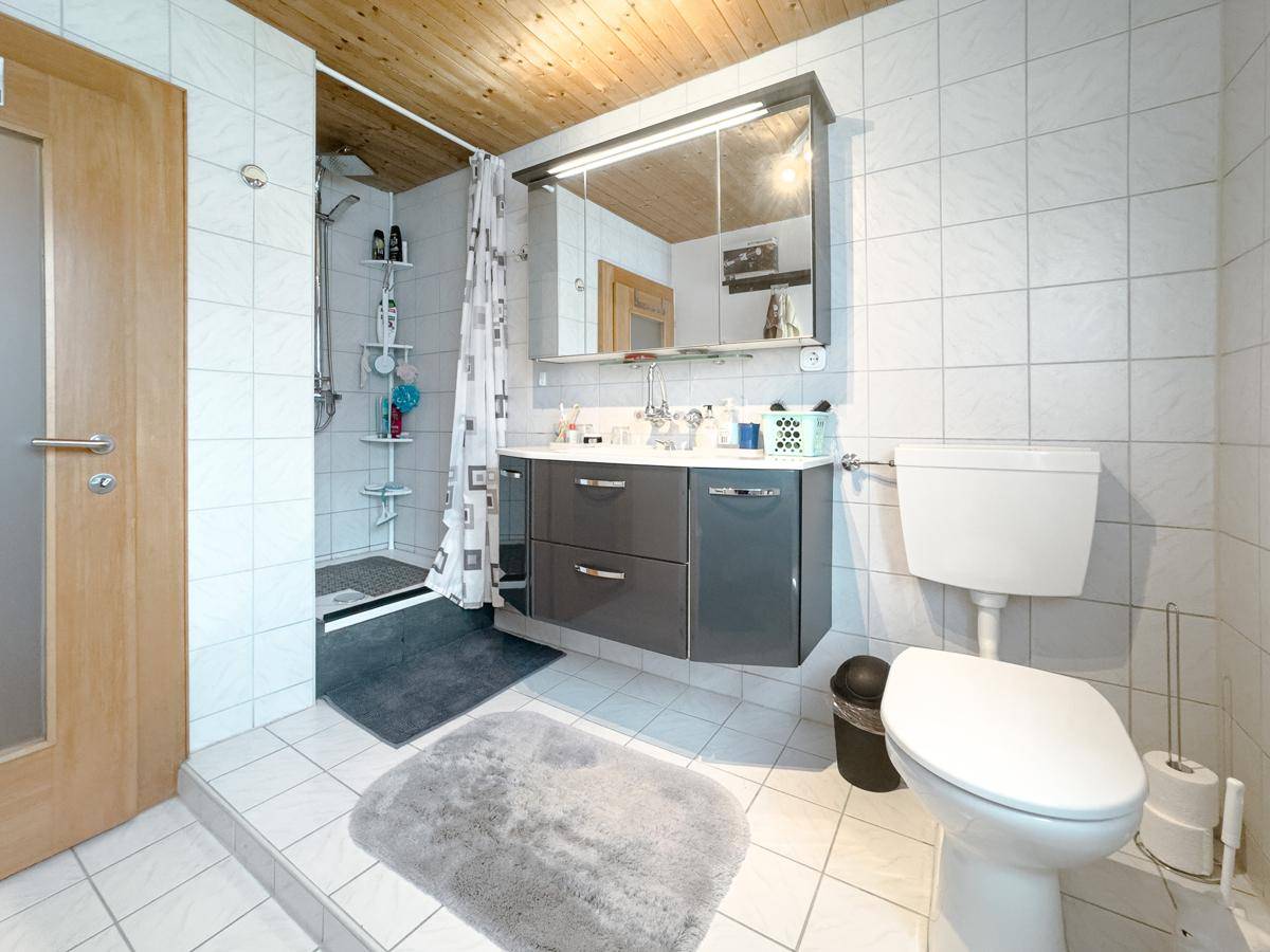 Modern gefliestes Badezimmer mit Dusche, Waschtisch und Holzdecke.