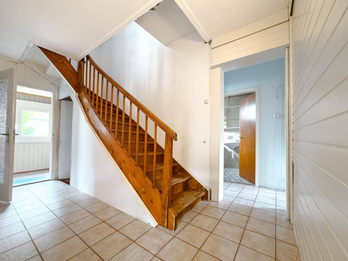 Geräumiger Flur mit Holztreppe und Fliesenboden, der die verschiedenen Etagen verbindet.