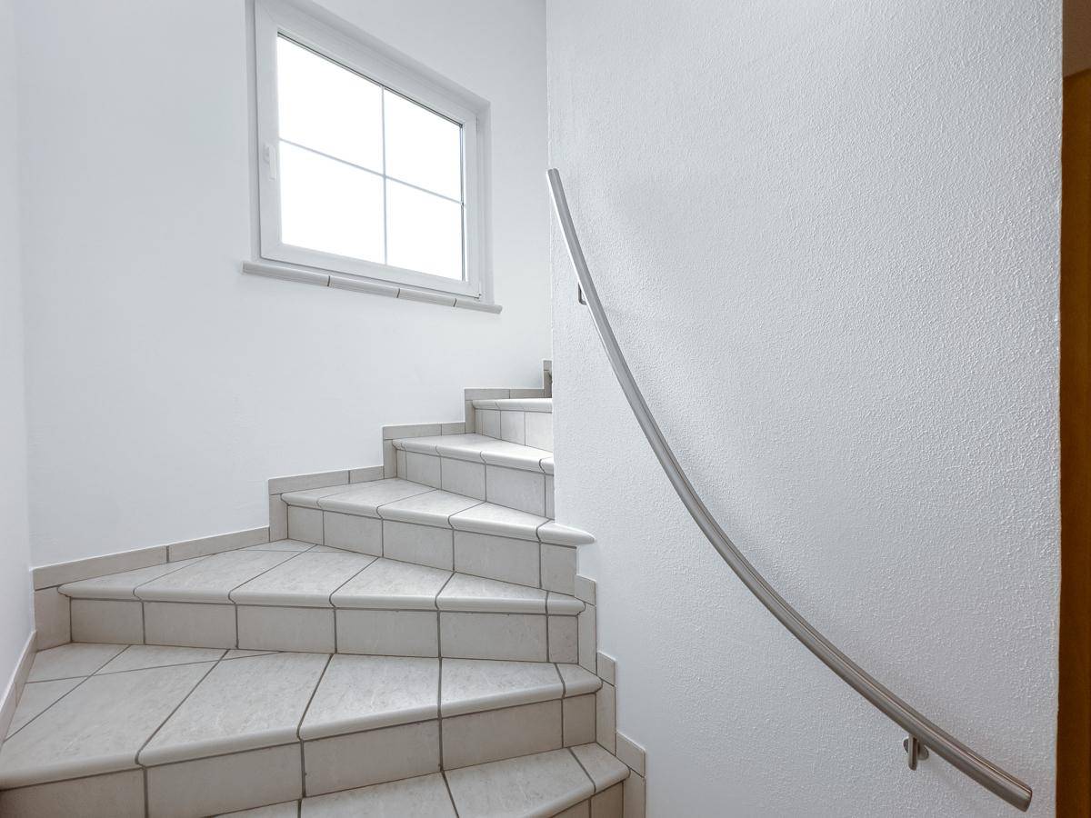 Heller Treppenaufgang mit Fliesenstufen, Handlauf und Fenster für natürliches Licht.