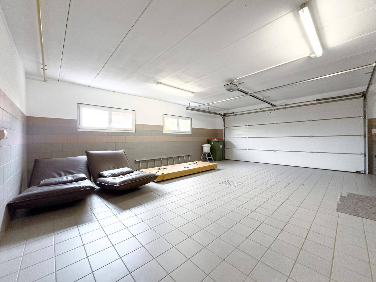 Innenansicht der Garage mit viel Platz, Fliesenboden und Tageslicht durch Fenster.
