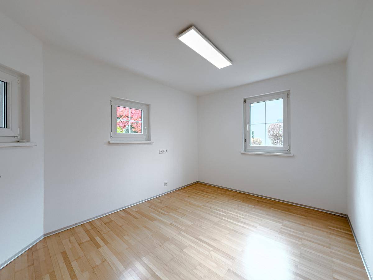 Helles, leeres Zimmer mit Parkettboden und zwei Fenstern, ideal als Schlaf- oder Arbeitszimmer.