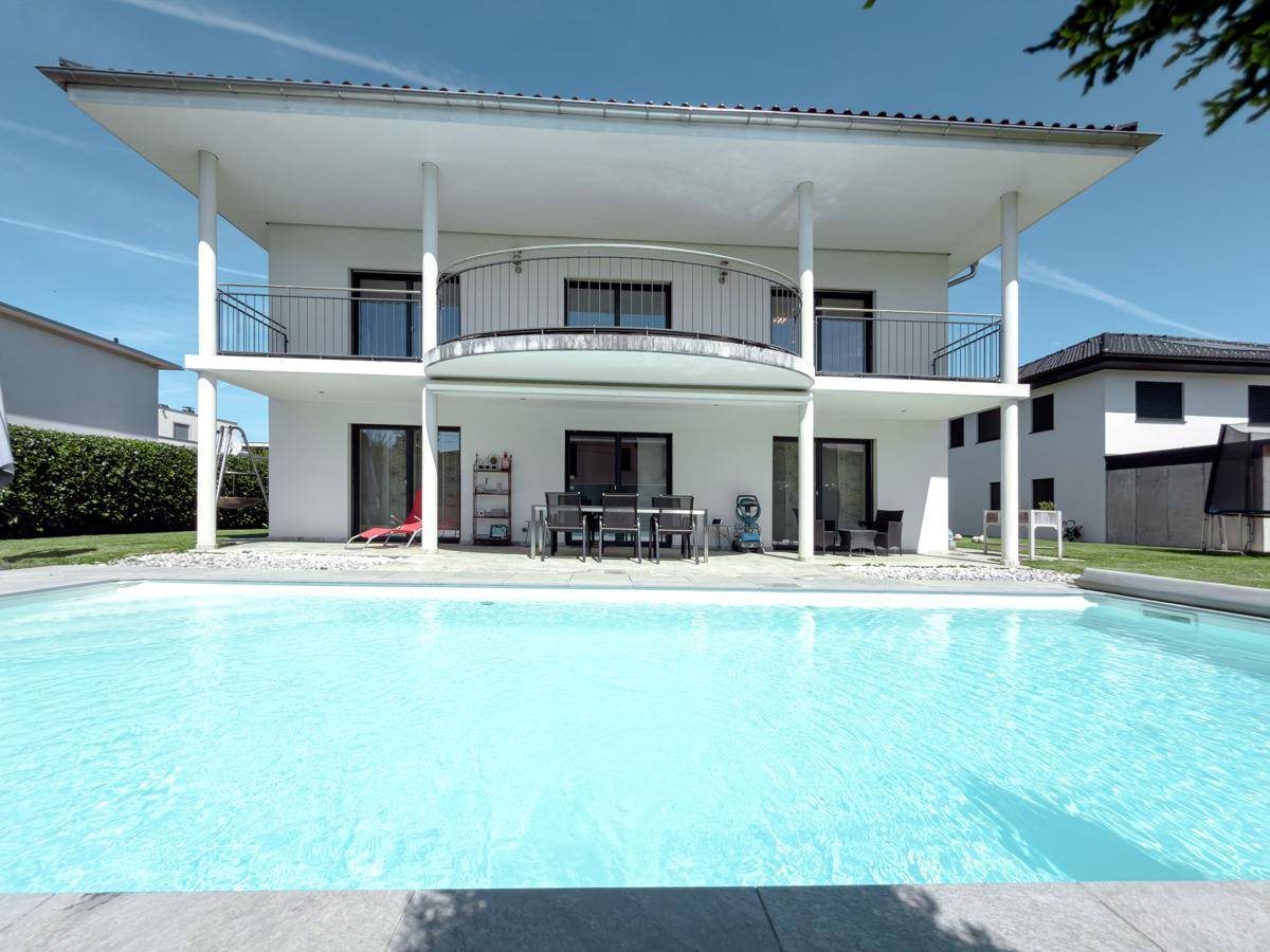 Rückseite des Hauses mit großem Pool und möblierter Terrasse unter blauem Himmel.