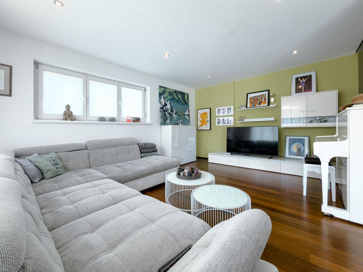 Gemütliches Wohnzimmer mit großem Ecksofa, Holzboden und moderner Unterhaltungselektronik.