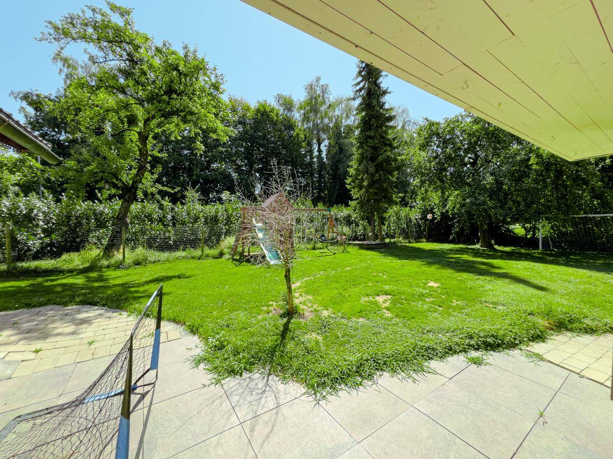 Gepflasterte Terrasse mit Blick auf den grünen Garten, Spielplatz und Sportmöglichkeiten im Freien.