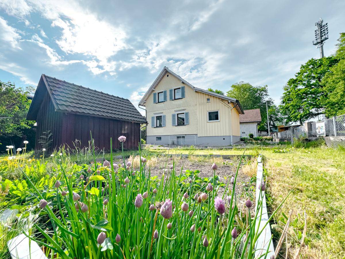 Gartenansicht des Hauses mit blühenden Kräutern im Vordergrund und Nebengebäude.
