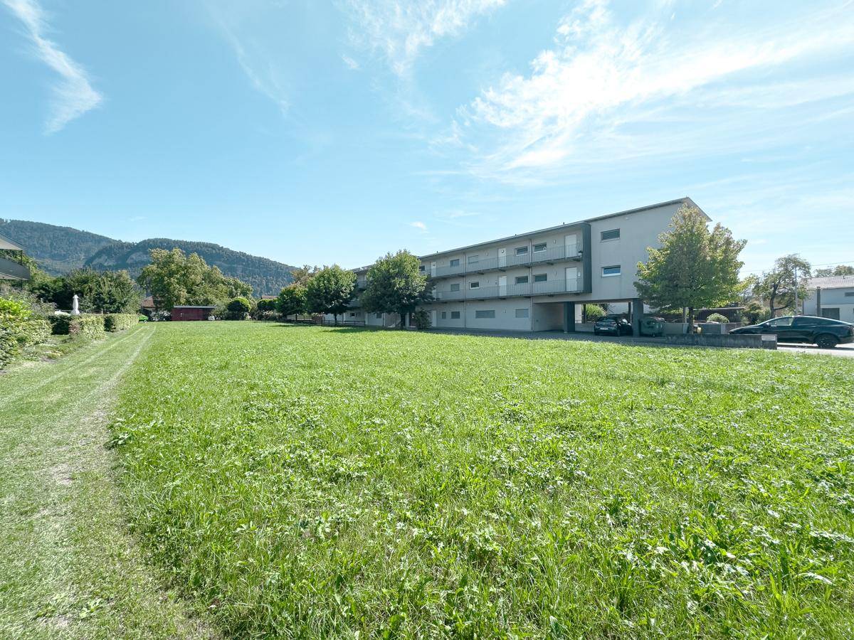 Grüne Wiese vor einem Wohngebäude mit Balkonen und Blick auf die hügelige Landschaft.