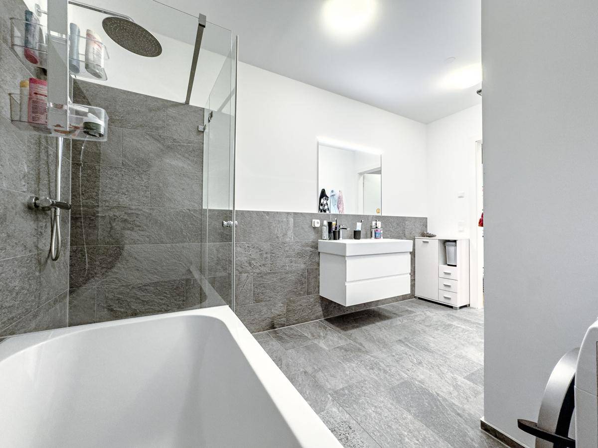 Modernes Badezimmer mit Badewanne, Regendusche, schwebendem Waschtisch und grauen Fliesen.