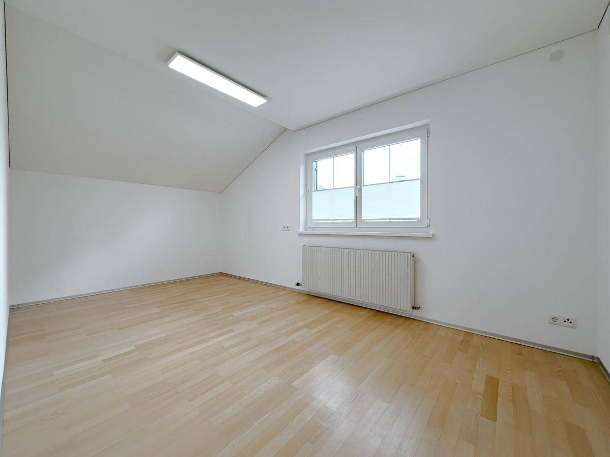 Geräumiges Zimmer im Dachgeschoss mit hellem Laminatboden und zwei Fenstern.