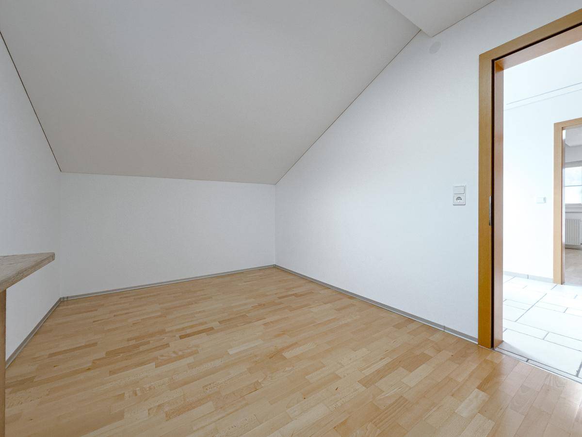 Ruhiges Zimmer im Dachgeschoss mit Parkettboden, weiß gestrichenen Wänden und Dachschräge.