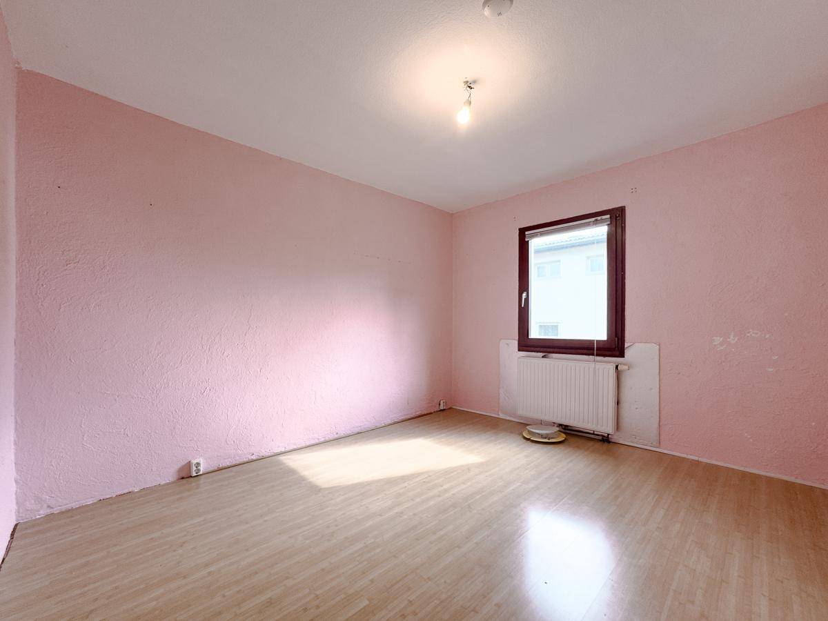 Schlafzimmer mit rosa Wänden, Laminatboden und Fenster, ideal für individuelle Einrichtung.