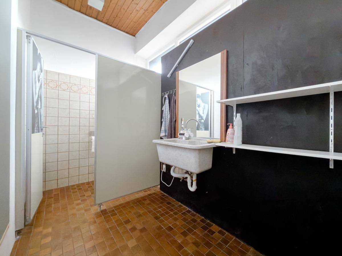 Badezimmer mit Waschbecken, Spiegel und einer Duschkabine, ausgestattet mit braunen Fliesen.