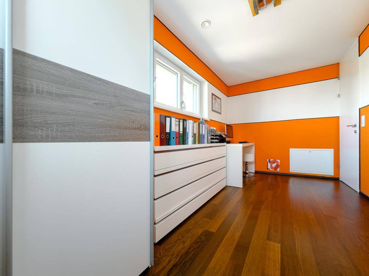 Modernes Arbeitszimmer mit orangefarbenen Akzentwänden, Schreibtisch und viel Stauraum.