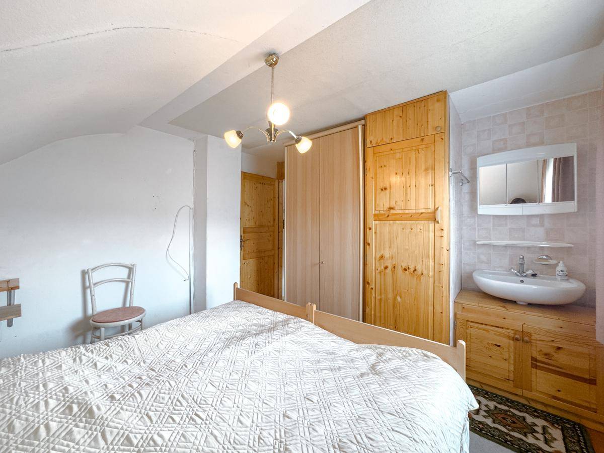 Schlafzimmer im Dachgeschoss mit Doppelbett, Holzschrank und integriertem Waschbecken.