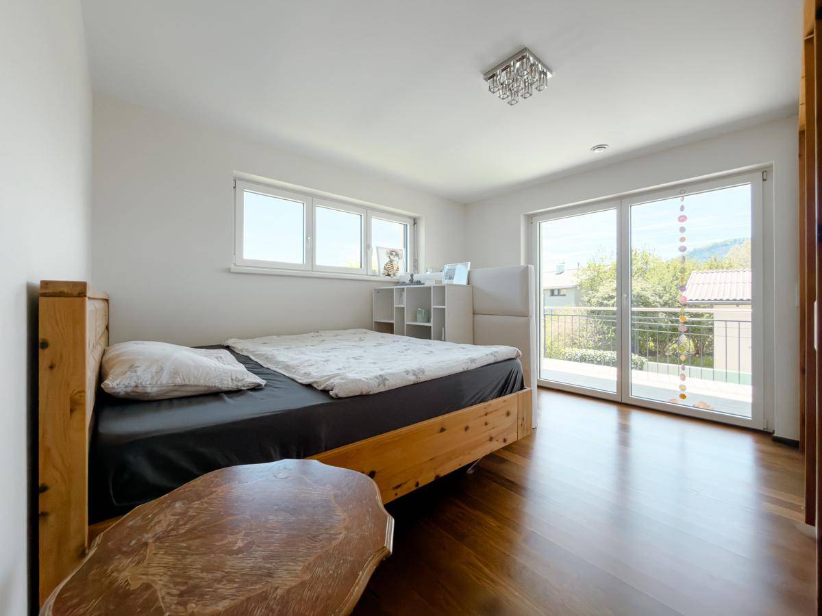 Schlafzimmer mit Holzbett, Parkettboden und Zugang zu einem Balkon.