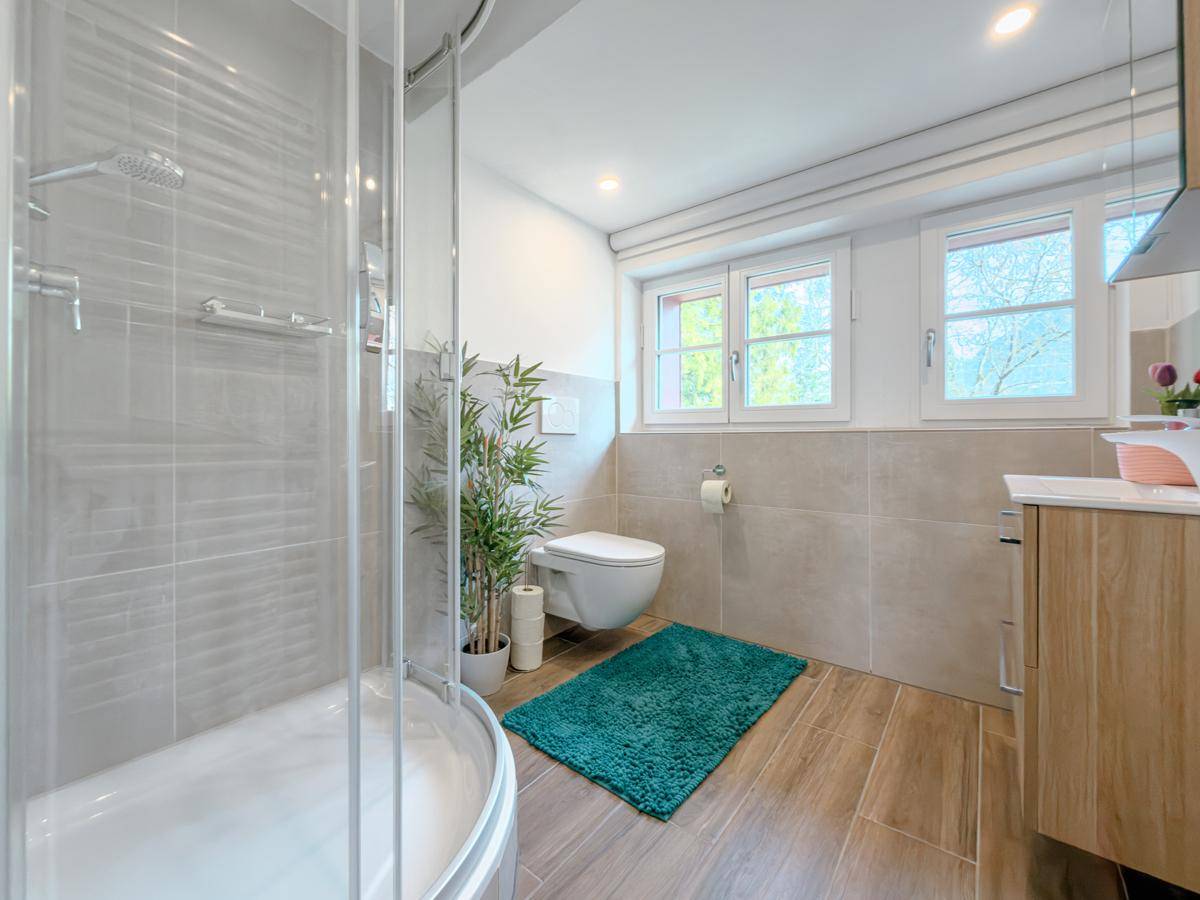 Modernes Badezimmer mit Duschkabine, Wand-WC und Holzoptikfliesen, hell und funktional.