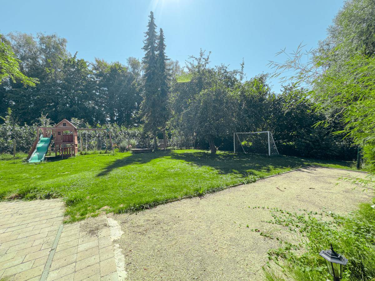 Weitläufiger Garten mit Spielplatz, Rasen, Bäumen und einem Fußballtor unter blauem Himmel.