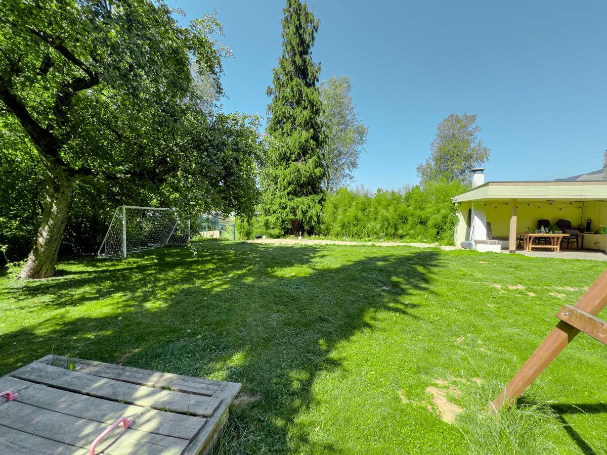 Weitläufiger Garten mit Sandkasten, Rasenfläche, Bäumen und einem Fußballtor für Kinderaktivitäten.