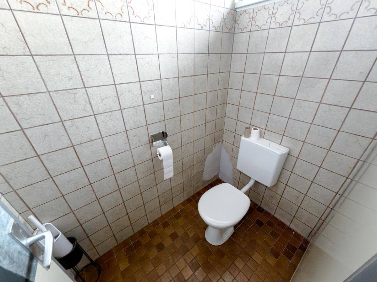 Kleiner Toilettenraum mit beigen Wandfliesen, braunem Boden und einer weißen Toilette.