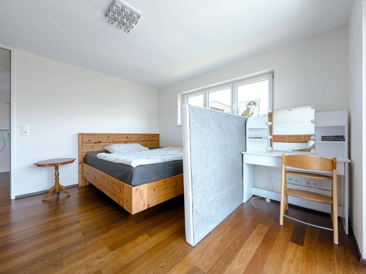 Helles Schlafzimmer mit Holzbett, Holzboden und einem Schminktisch am Fenster.