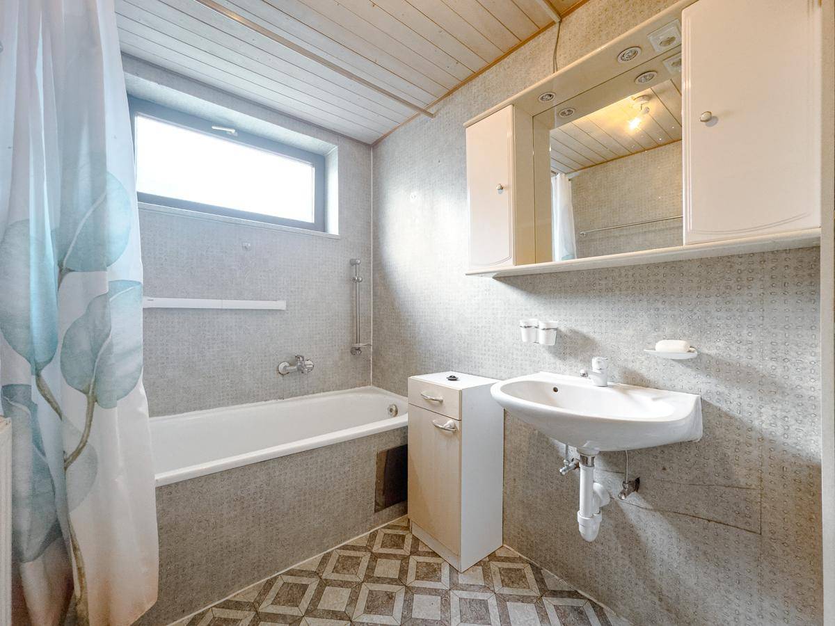 Badezimmer mit Badewanne, Waschbecken, Spiegelschrank und Fenster für Tageslicht.