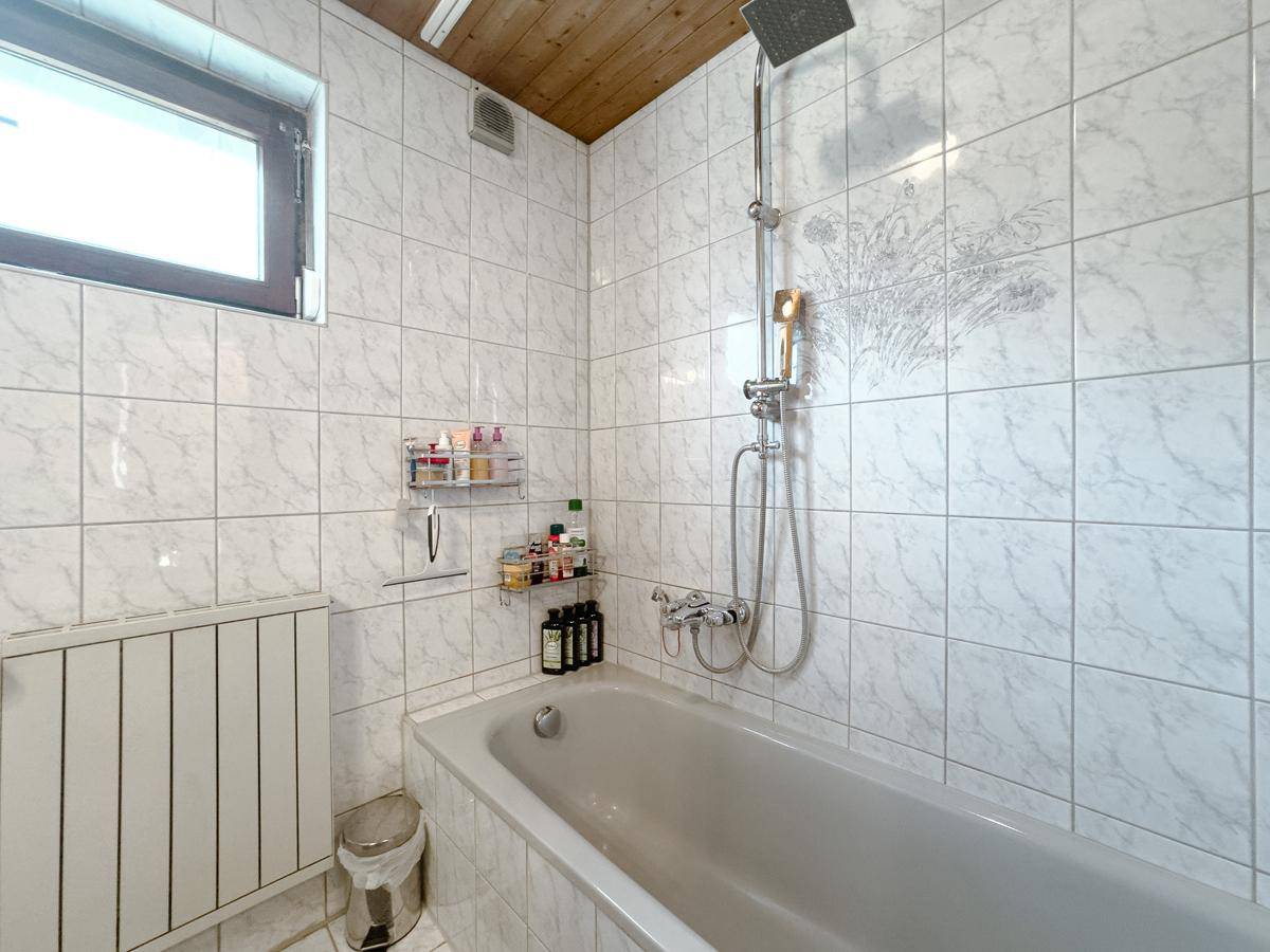 Badezimmer mit Badewanne, Duschfunktion, weißen Fliesen und Fenster für Tageslicht.
