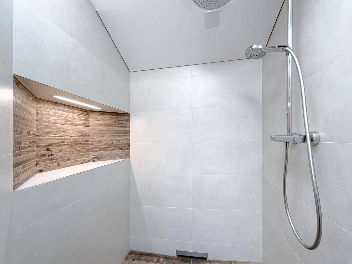 Geräumige Dusche mit Regenduschkopf und integrierter Ablage in Holzoptik.