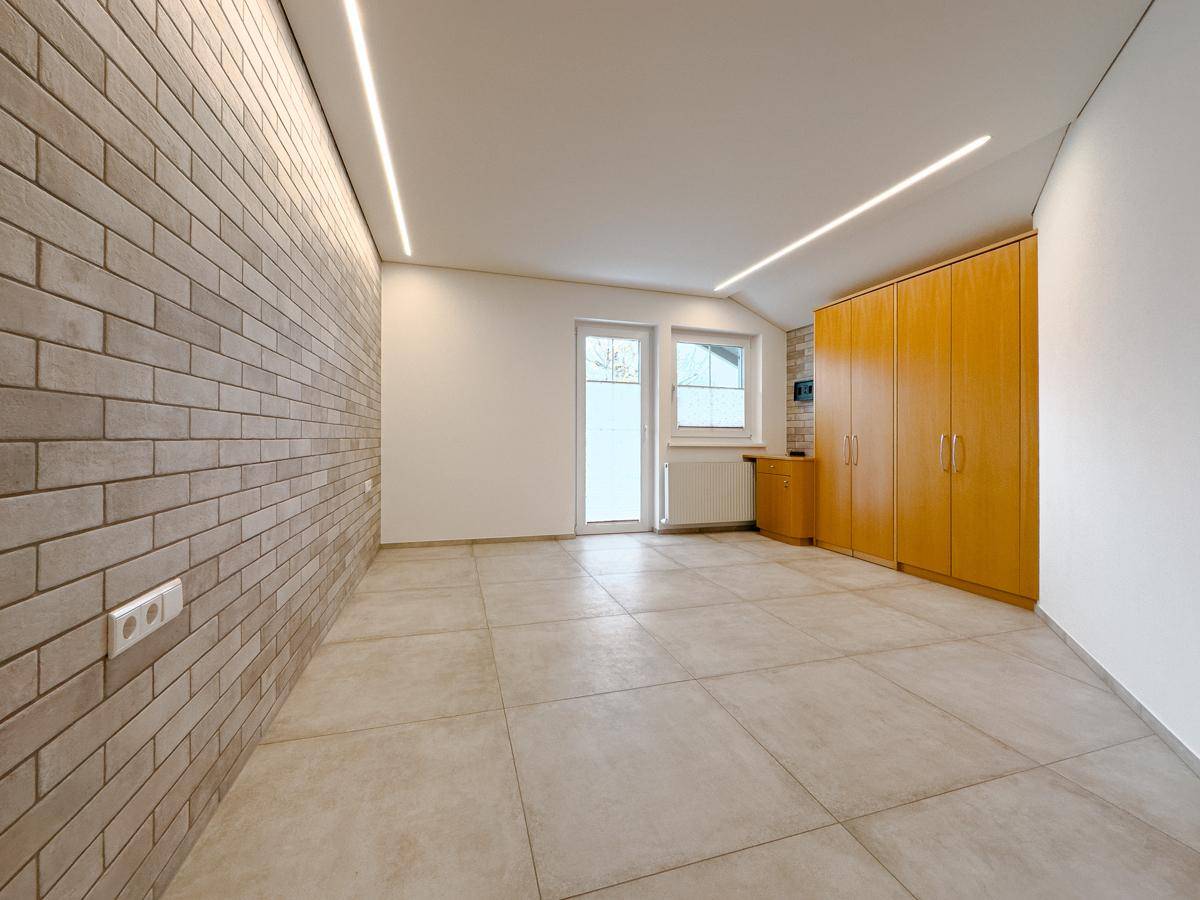 Geräumiger Raum mit Ziegelwand, Fliesenboden und integrierten Holzschränken.