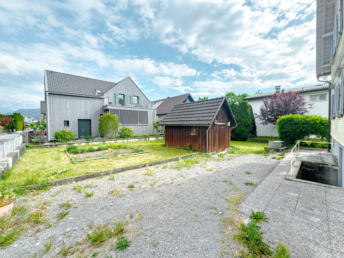 Gartenbereich hinter dem Haus mit Rasen, Pflanzbeeten und einem kleinen Holzschuppen.