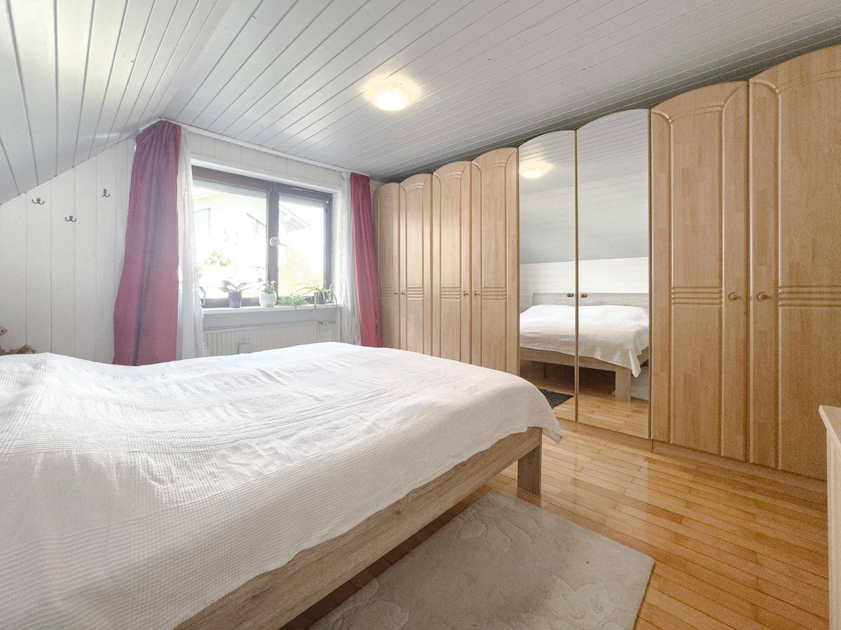 Gemütliches Schlafzimmer im Dachgeschoss mit Holzboden und großem Spiegelschrank.