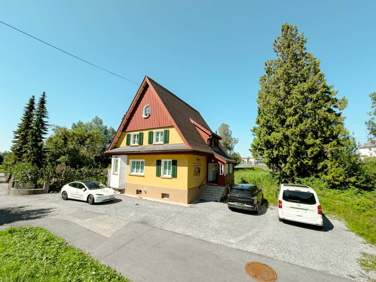 Charmantes Einfamilienhaus mit gelber Fassade, rotem Satteldach und grünen Fensterläden in ländlicher Umgebung.