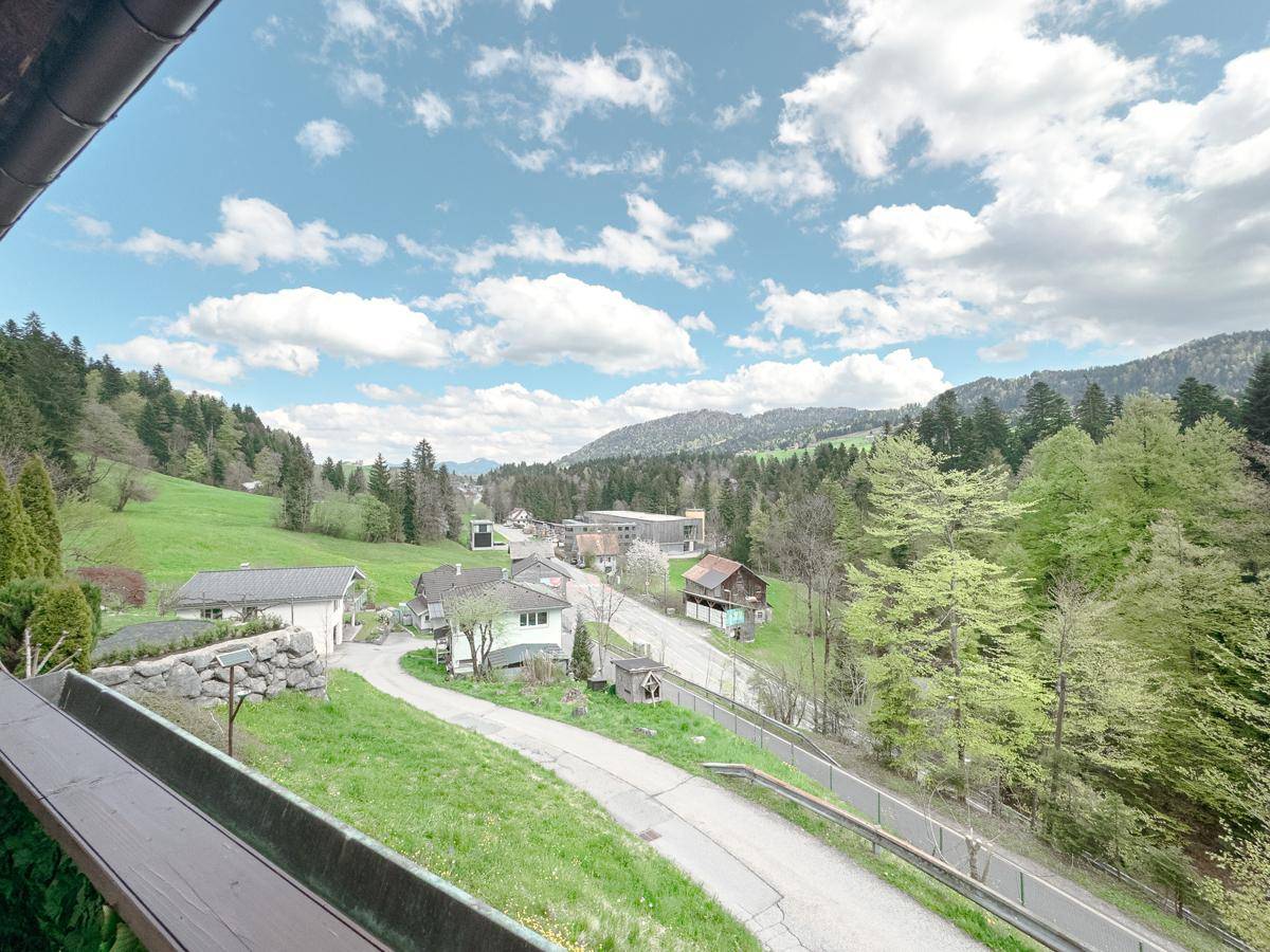 Weitläufiger Ausblick vom Balkon über ein grünes Tal mit Häusern und bewaldeten Hügeln.