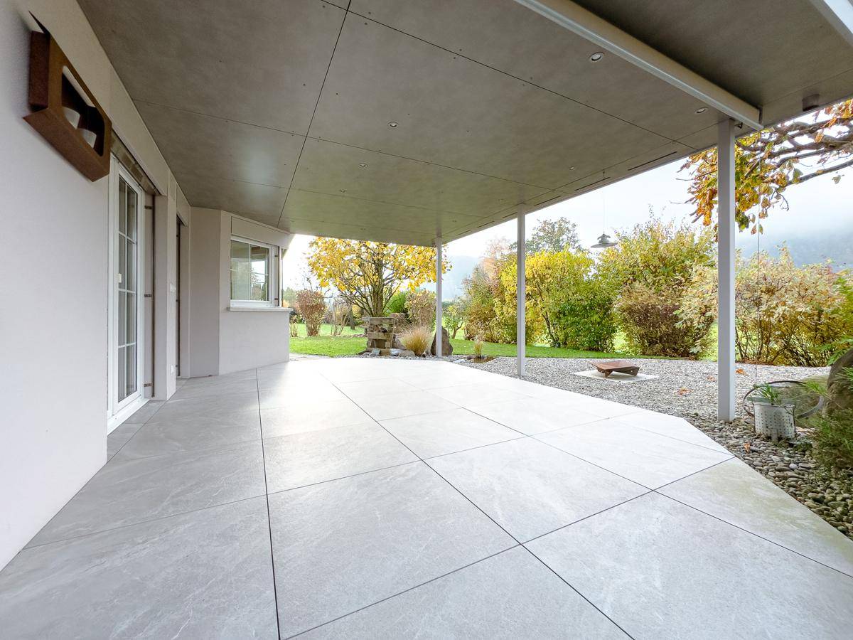 Helle überdachte Terrasse mit großformatigen Fliesen und Zugang zum Gartenbereich.