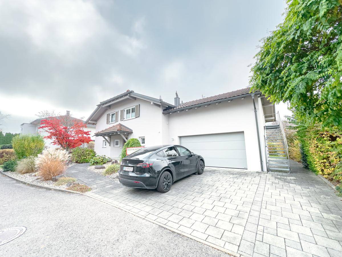 Seitenansicht des Hauses mit großer Garage, gepflasterter Einfahrt und Außentreppe.