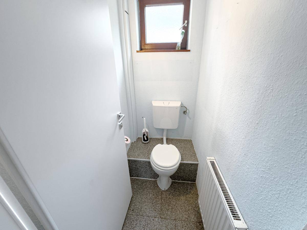 Separates WC mit Toilette, Heizkörper und kleinem Fenster für Belüftung.