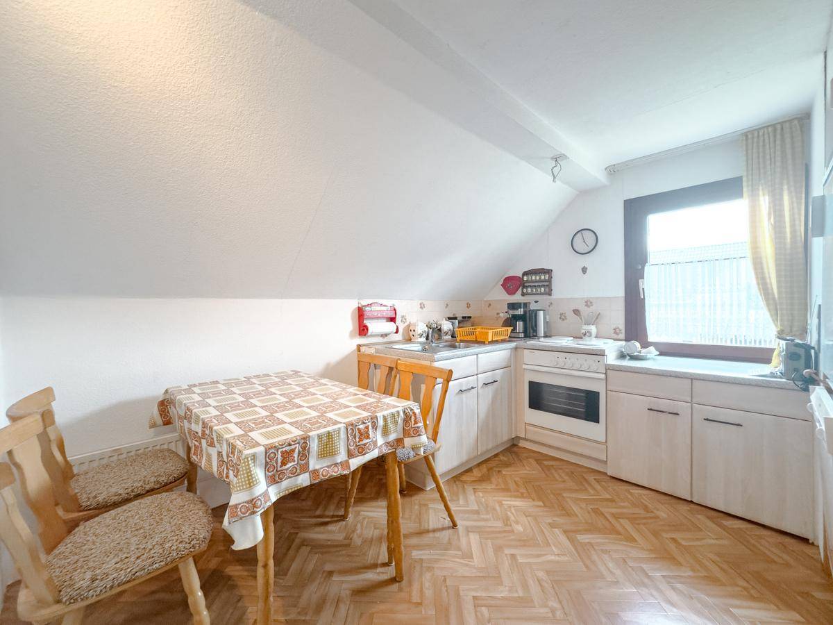 Gemütliche Küche im Dachgeschoss mit Esstisch, Einbauschränken und Fenster.