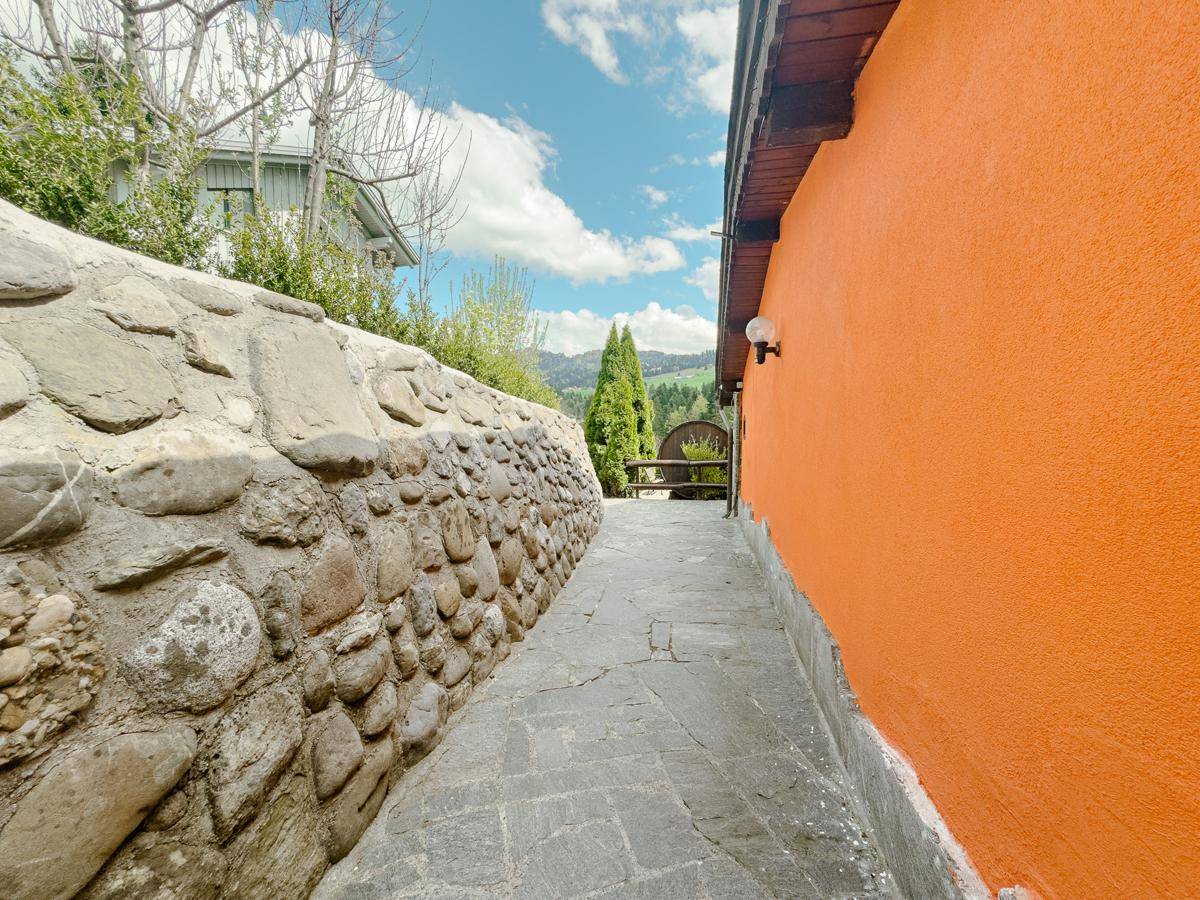 Steinweg entlang einer Natursteinmauer und dem Haus mit orangefarbener Fassade.