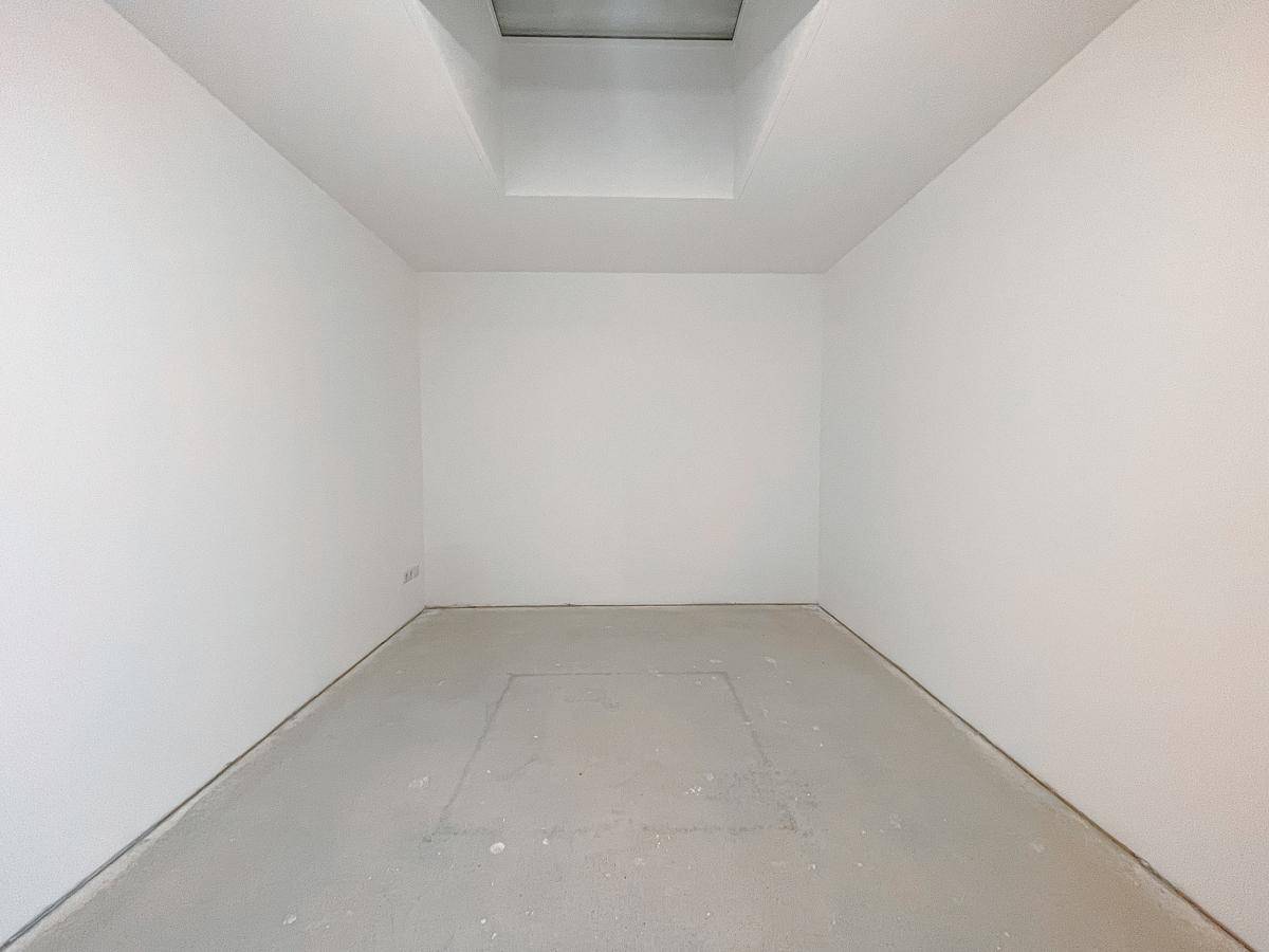 Leerer Raum mit weiß gestrichenen Wänden, Betonboden und einem Oberlicht für natürliches Licht.